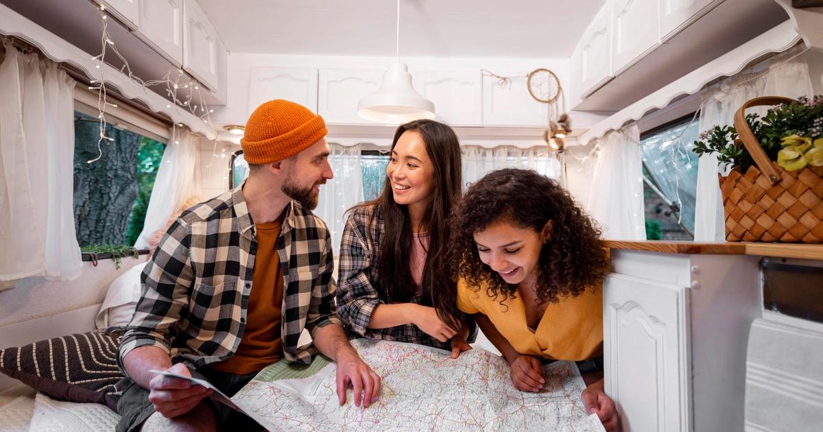 Three people reviewing a map inside a modern RV, planning a camping trip or campground route.