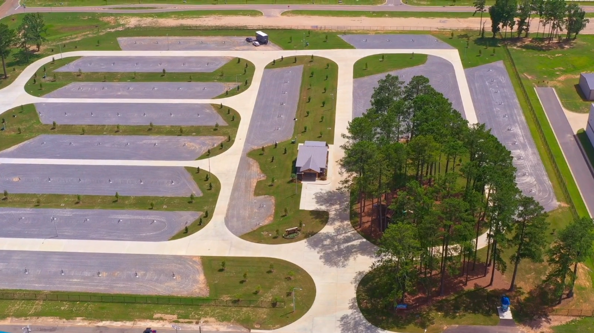 Aerial view of Piney Hills RV park showing multiple paved RV sites with green grass strips, trees, and a central building surrounded by organized parking areas.