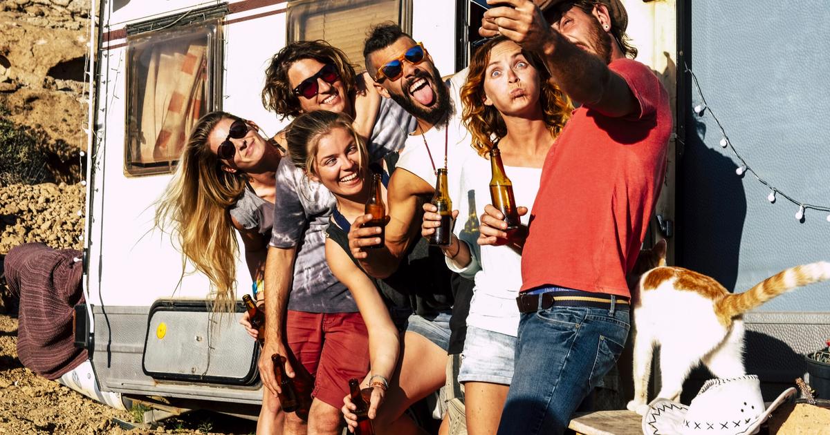 Group of friends celebrating outside a travel trailer in a desert setting, holding beverages and enjoying recreational activities at an RV campsite.