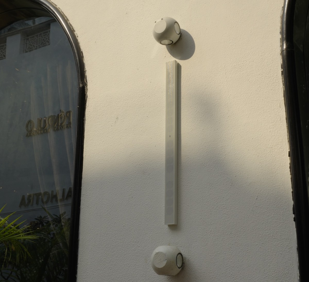 XSCACE QuadCane speaker mounted on a textured stucco restaurant facade between arched windows