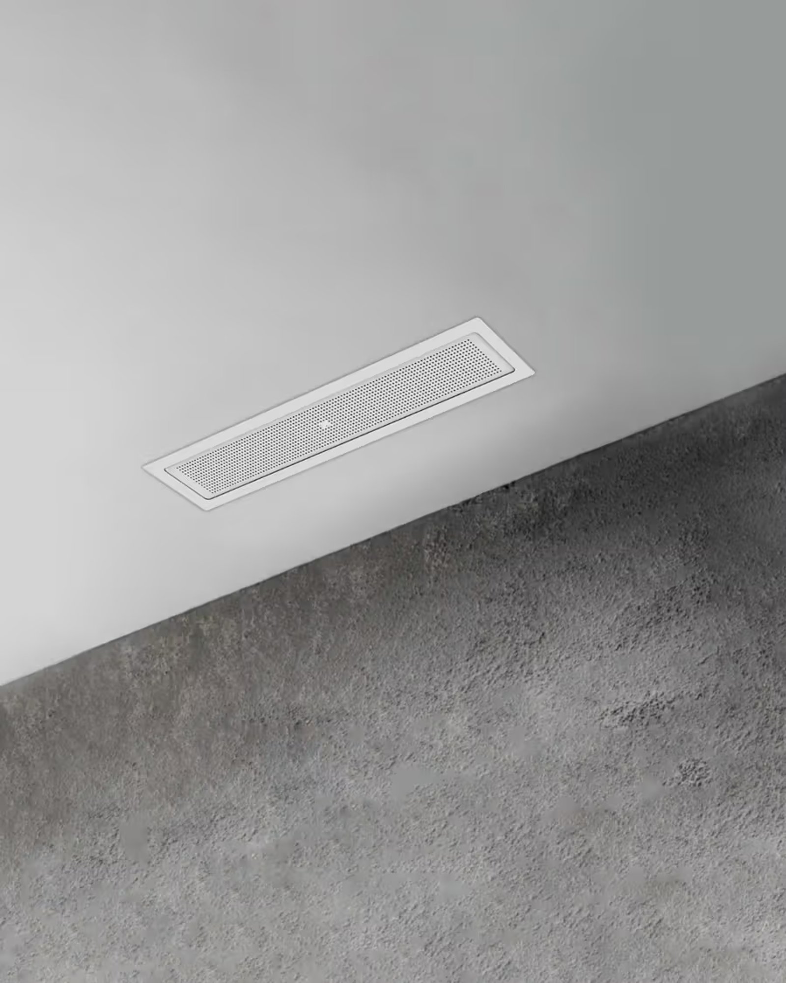 An XSCACE Ghost 2.0 slim in-ceiling speaker recessed flush into a white plaster ceiling, its narrow rectangular grille sitting almost level with the surface above a textured concrete wall
