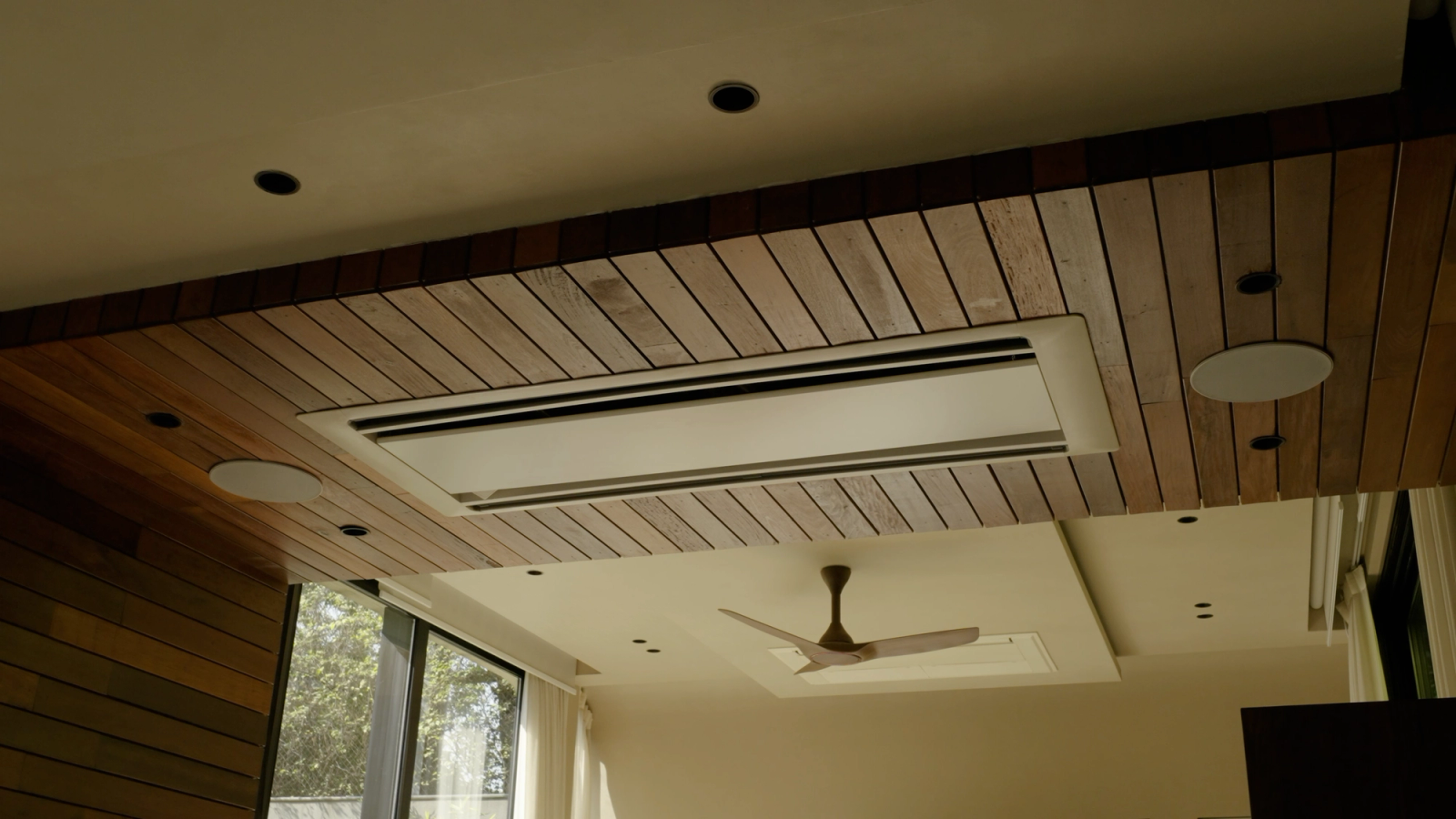 A white round XSCACE Aspen 6 in-ceiling speaker set into a slatted timber ceiling — 209mm cutout, 6-inch driver, reaching 50Hz