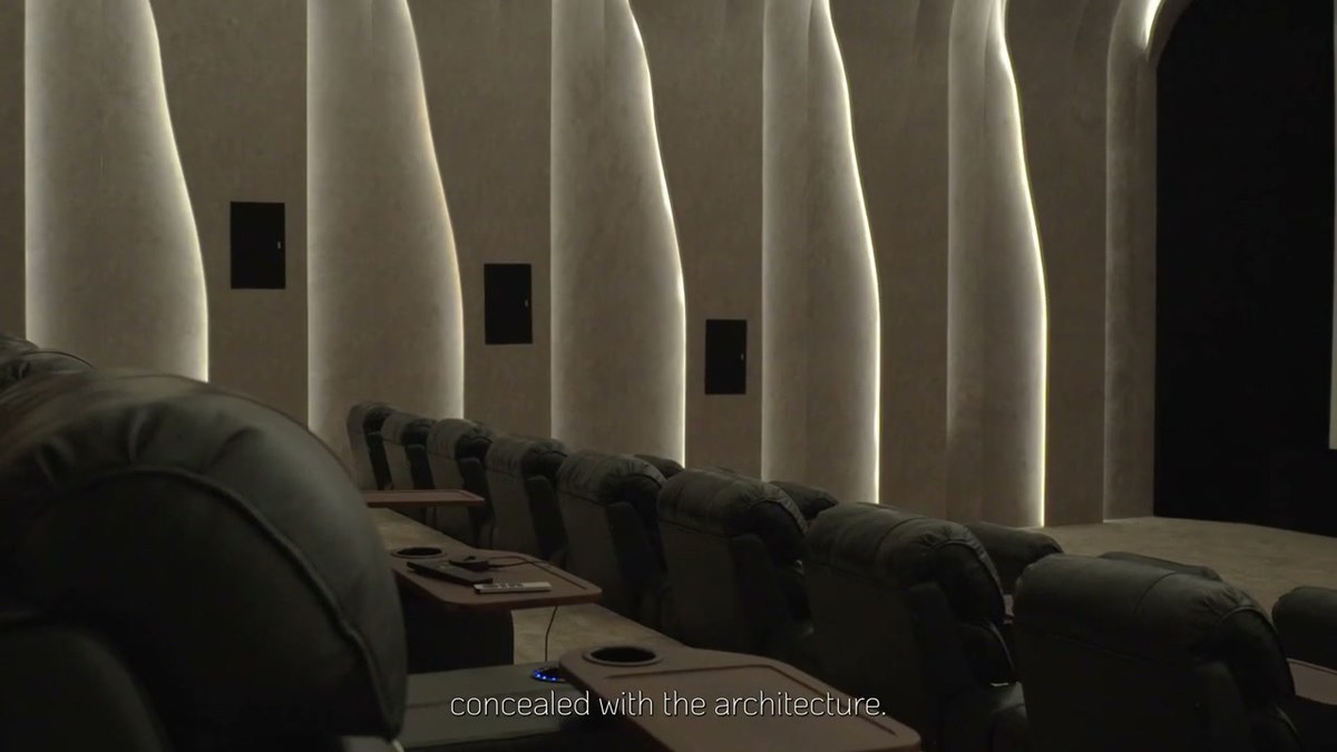 Two tiered rows of cinema seating inside a curved acoustic shell, with speaker apertures set into the wall panels