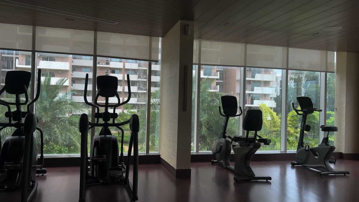 QuadCane slim array speakers in a fully glazed clubhouse gym, mounted on textured plaster piers between floor-to-ceiling windows above a dark timber floor