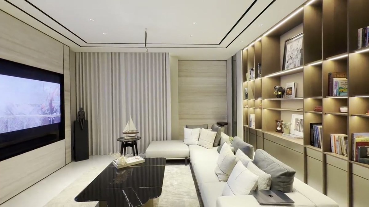 A media lounge with a wall-recessed television, a custom XSCACE LCR soundbar beneath it, a sectional sofa and a full-height illuminated bookcase