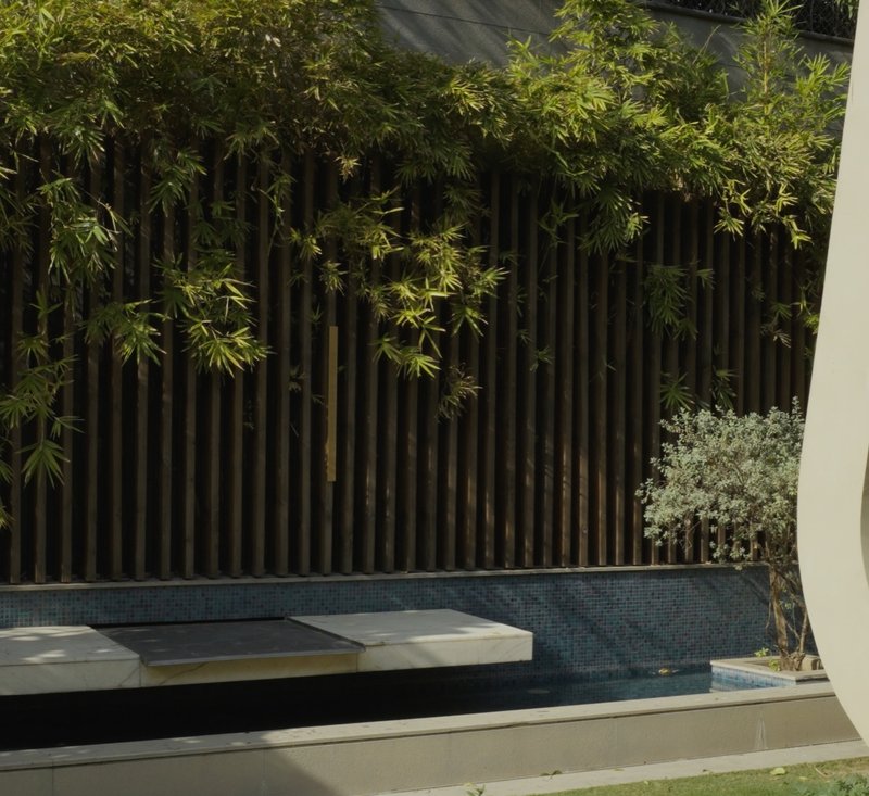 XSCACE QuadCane speaker mounted on a dark timber privacy fence beside a mosaic-tiled swimming pool