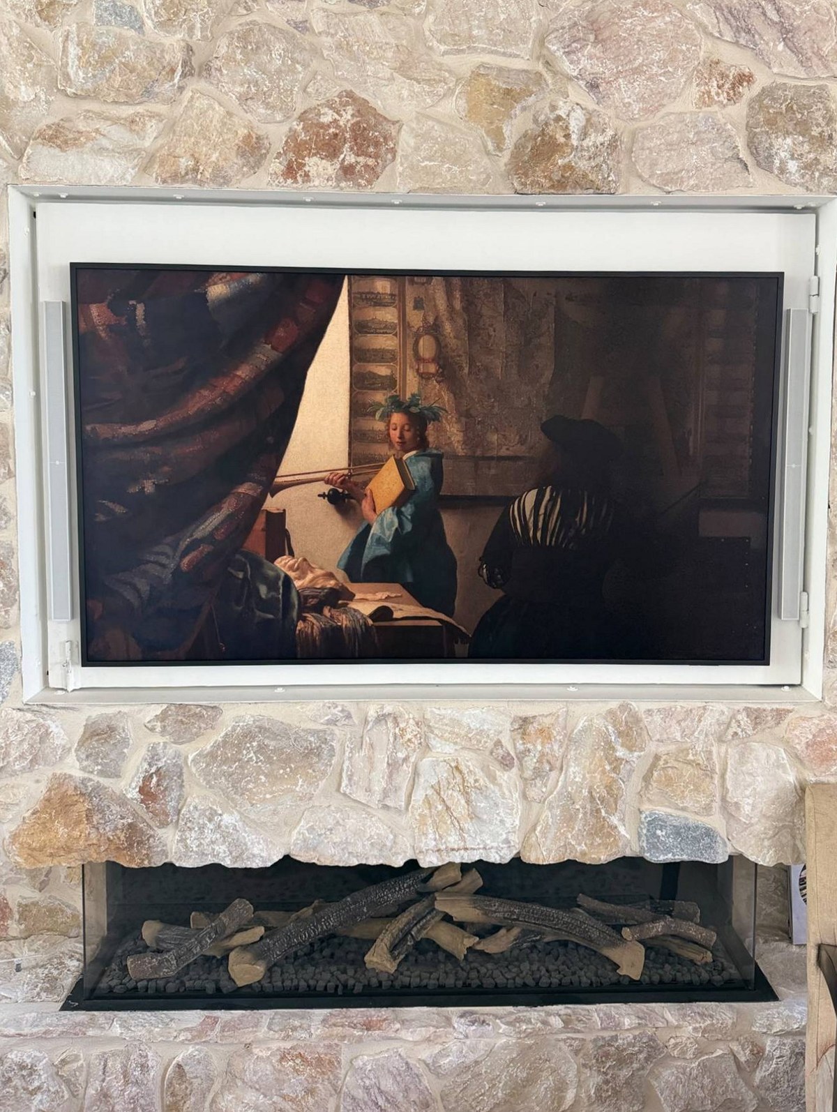 A limestone fireplace wall seen vertically, with a recessed television above a linear gas fire and the stone hearth below