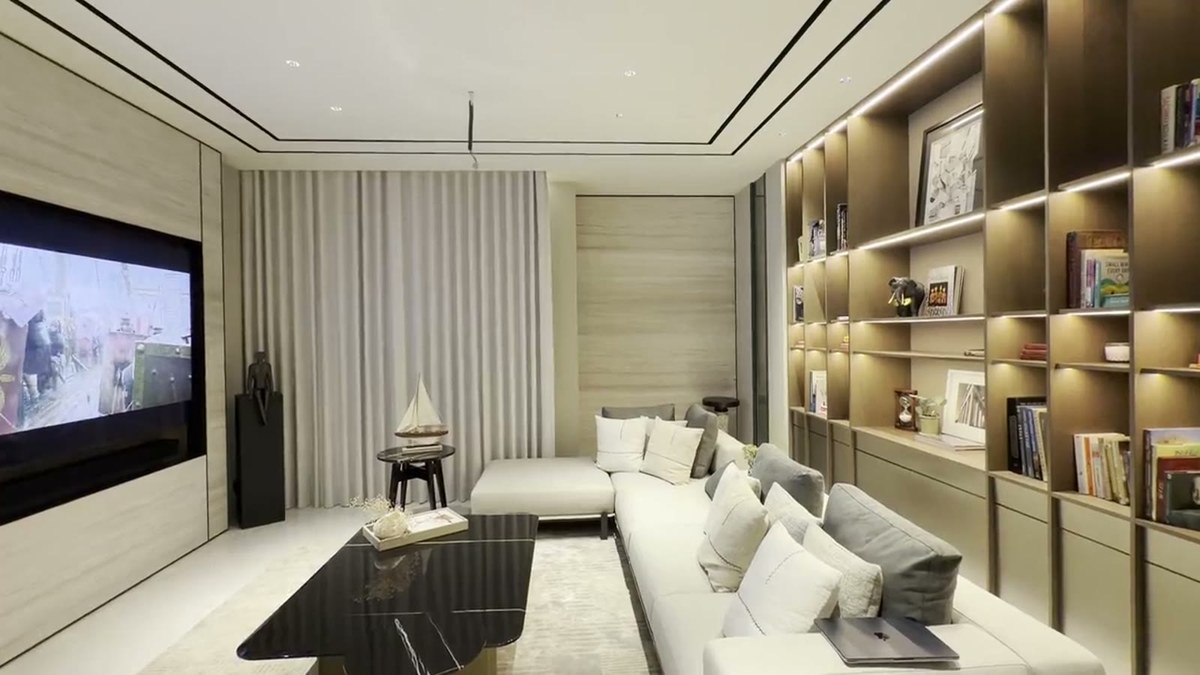 A media lounge with a wall-recessed television, a custom XSCACE LCR soundbar beneath it, a sectional sofa and a full-height illuminated bookcase