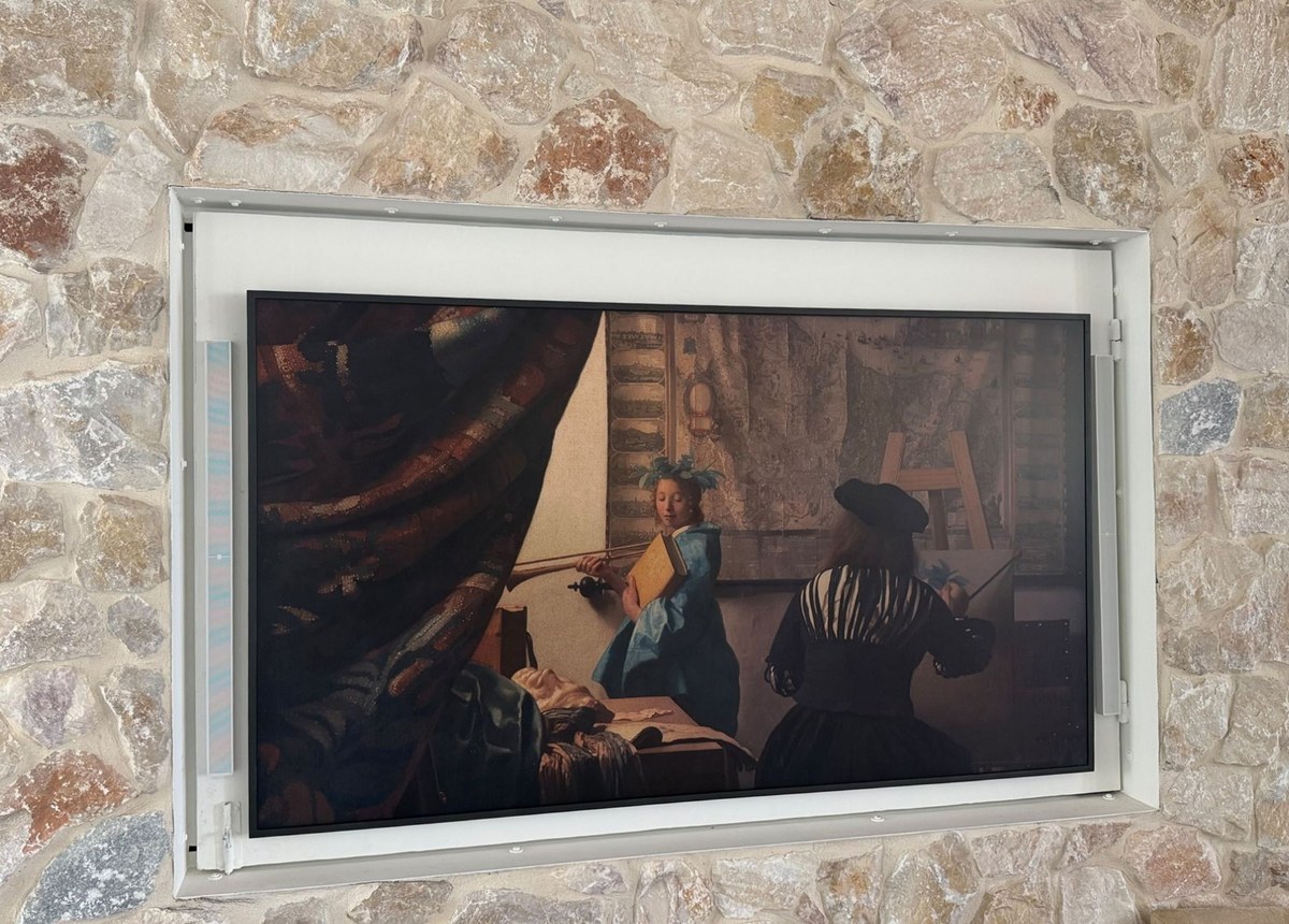 A limestone fireplace wall with a recessed television flanked by two white XSCACE QuadCane slim array speakers mounted vertically in the frame reveal
