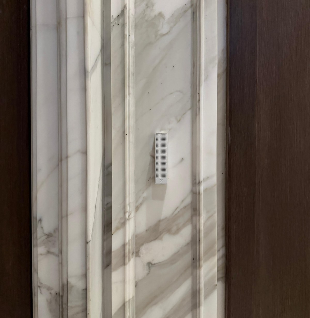 XSCACE Bonsai speaker on a fluted Calacatta-style marble pilaster in a lift lobby