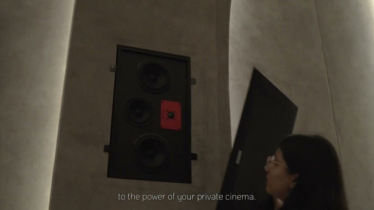 An installer lifting a grille clear of a wall aperture during commissioning, showing the speaker set behind the finish
