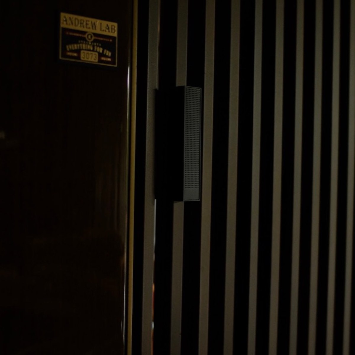 XSCACE Bonsai speaker in black finish on a fluted slat wall in a dimly lit games room