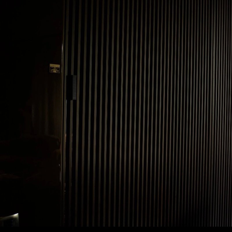XSCACE Bonsai speaker in black finish on a fluted slat wall in a dimly lit games room