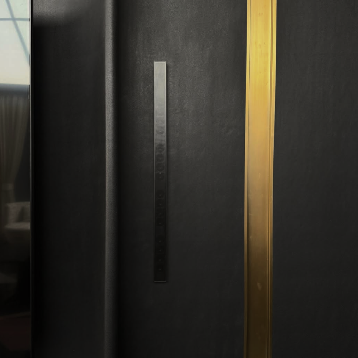 An ultra-slim XSCACE architectural line array speaker in a matte black finish, vertically surface-mounted on a dark textured accent wall next to a luxury champagne gold trim