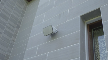 An XSCACE Camphor 8 all-weather outdoor patio speaker securely bracket-mounted horizontally to a wooden architectural pillar in a modern industrial-style outdoor seating environment.