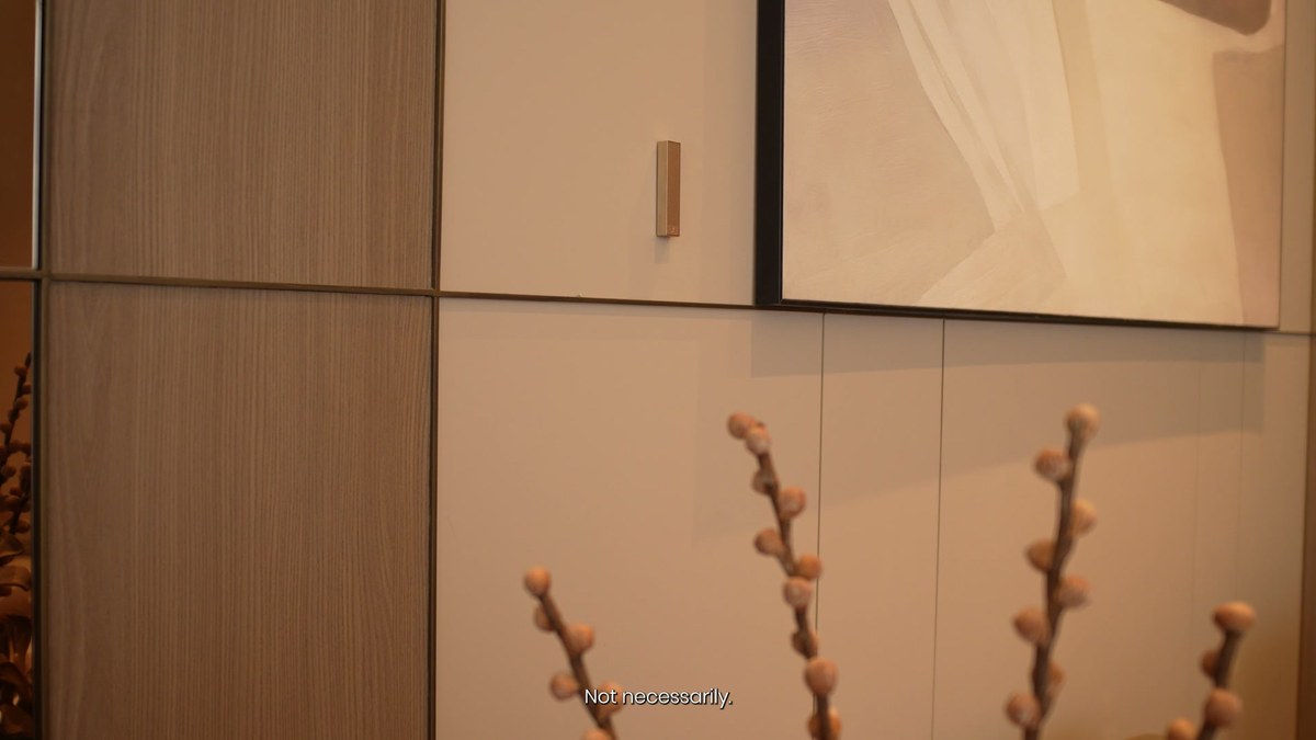 A white XSCACE Bonsai slim array speaker on a light wall panel beside a vase of blossom branches