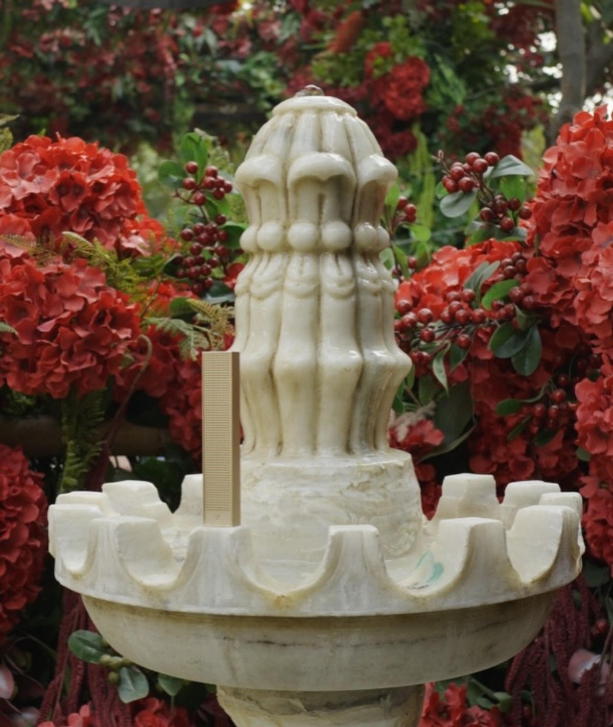 XSCACE Bonsai speaker mounted on a carved marble garden fountain surrounded by floral decor