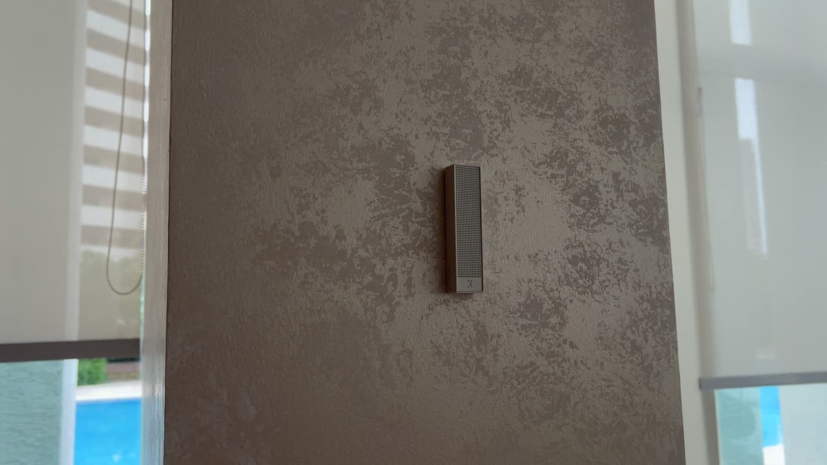 A white XSCACE Bonsai mini slim array on a textured plaster pier in a clubhouse book café, with the pool terrace visible through floor-to-ceiling glazing