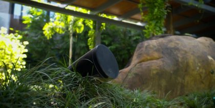 The XSCACE Spirea outdoor landscape speaker mounted via its rust-proof ground spike, blending discreetly into a vibrant garden bed of purple flowers to deliver seamless outdoor audio.