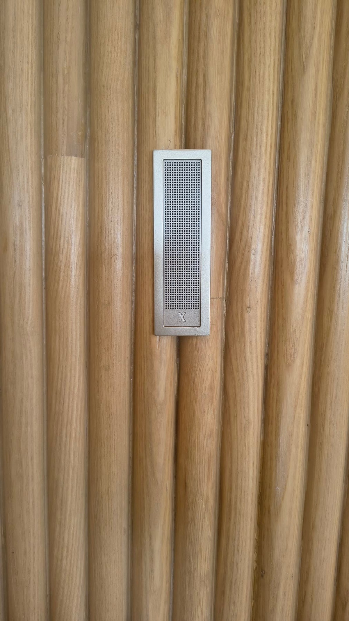 A Bonsai In-Ceiling In-Wall speaker flush-mounted in a fluted timber wall, grille finished to match the timber