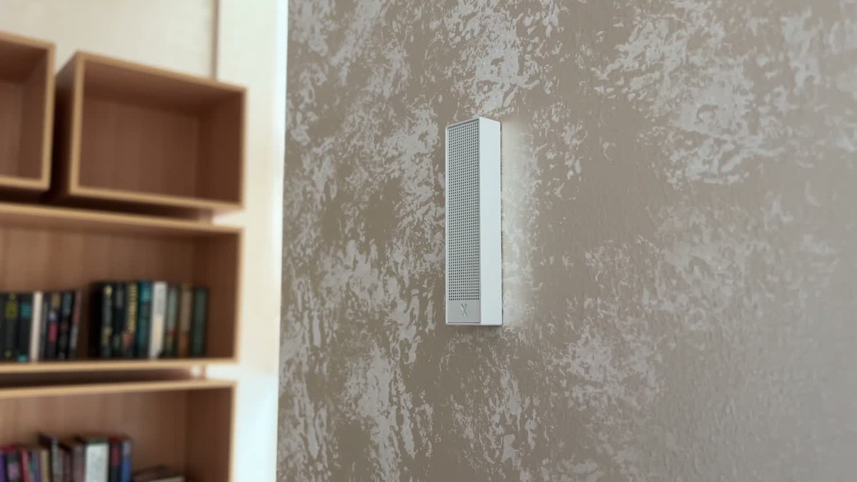 A white XSCACE Bonsai mini slim array on a textured plaster pier, with oak library shelving and books behind it in a clubhouse book café