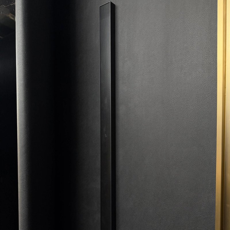 XSCACE QuadCane speaker mounted on black leather wall panelling beside a brass inlay strip