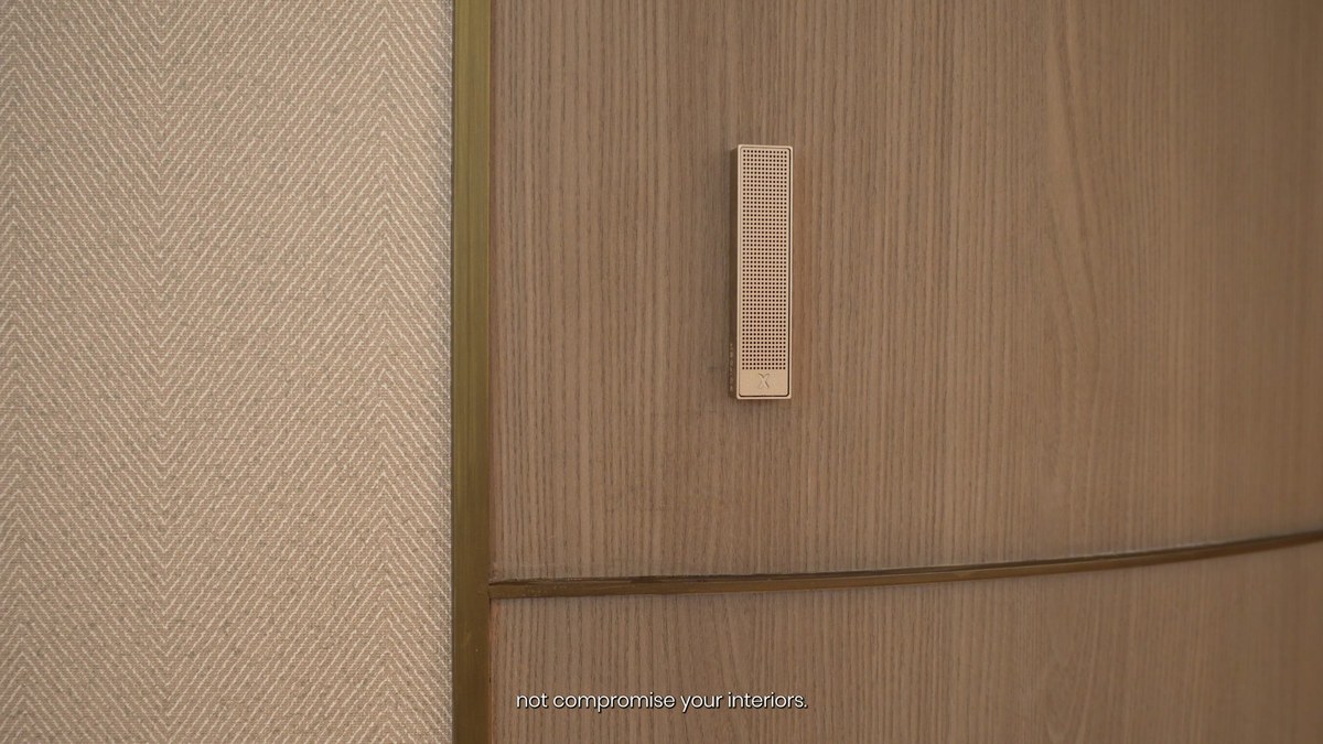 A white XSCACE Bonsai slim array speaker on a grey herringbone wall panel beside a timber-veneer panel
