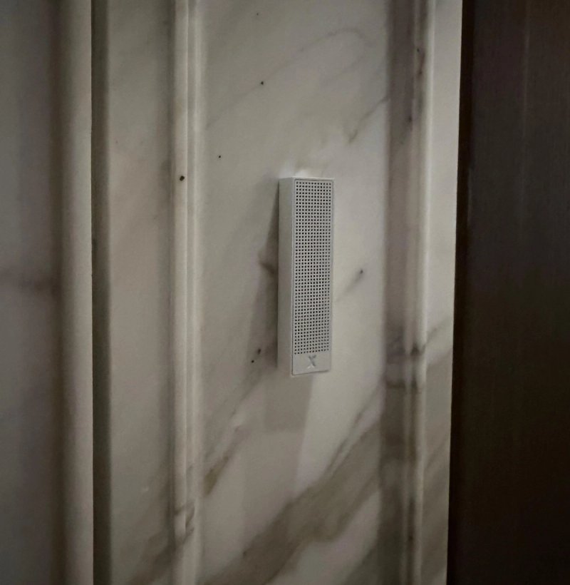XSCACE Bonsai speaker on a fluted Calacatta-style marble pilaster in a lift lobby