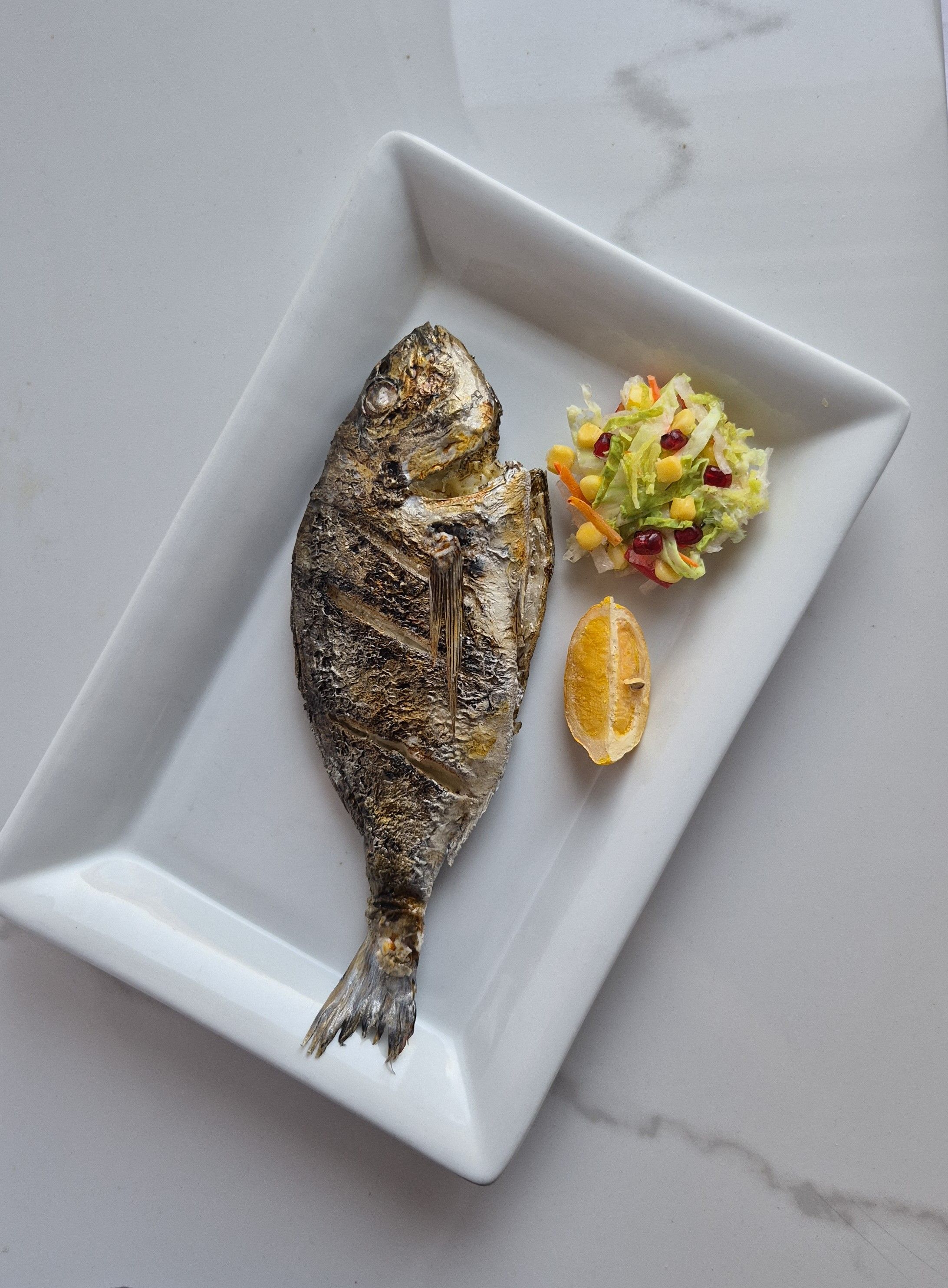 El yapımı ızgara çipura replikası, salata ve limonla tabak sunumu