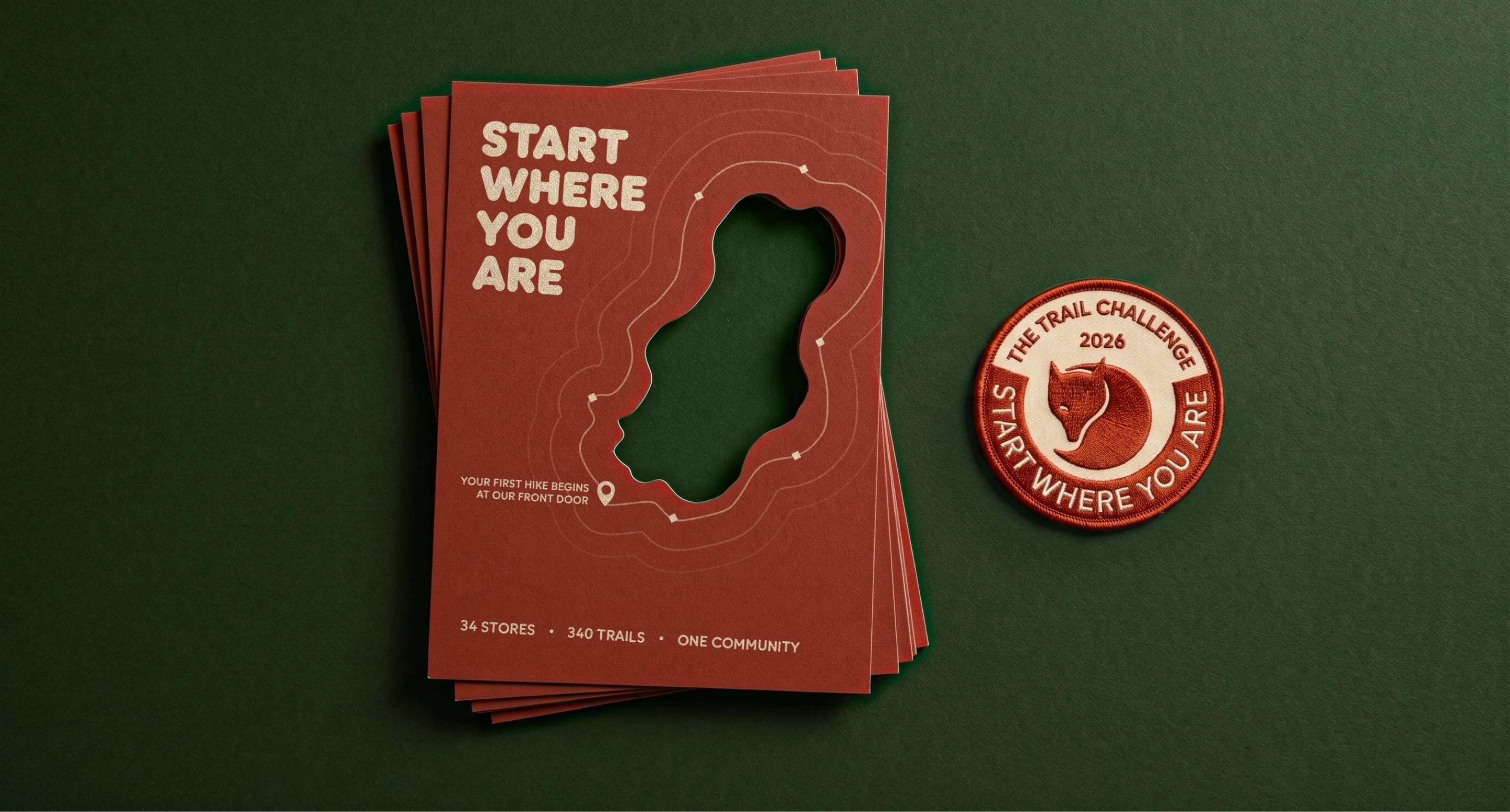 Stack of pin red flyers with an organic die-cut shape, next to three Trail Challenge patches on a forest green surface.