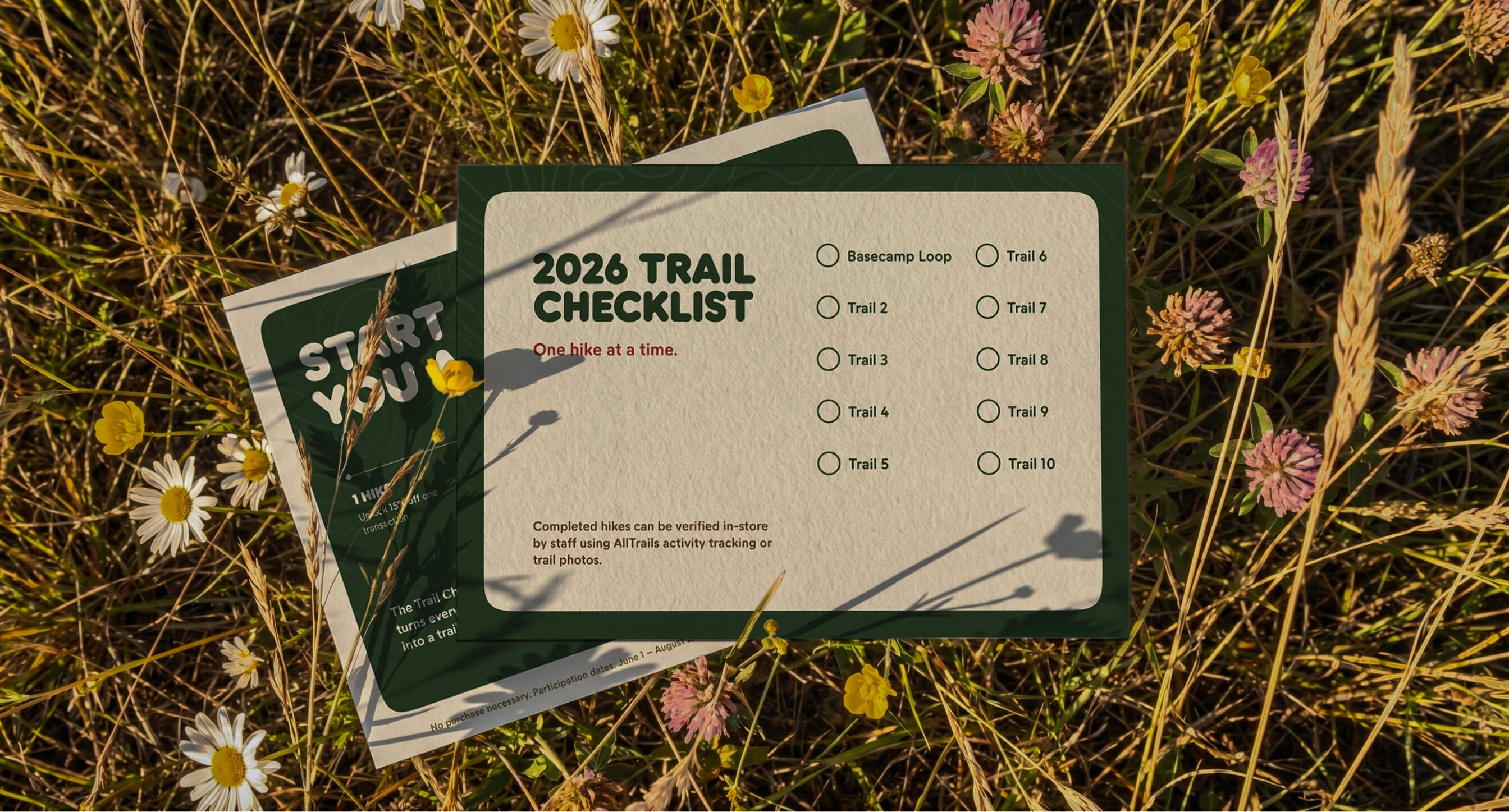 Two Nature Guide Postcards laid in a wildflower meadow, one face up showing the front, the other showing the trail checklist on the back.