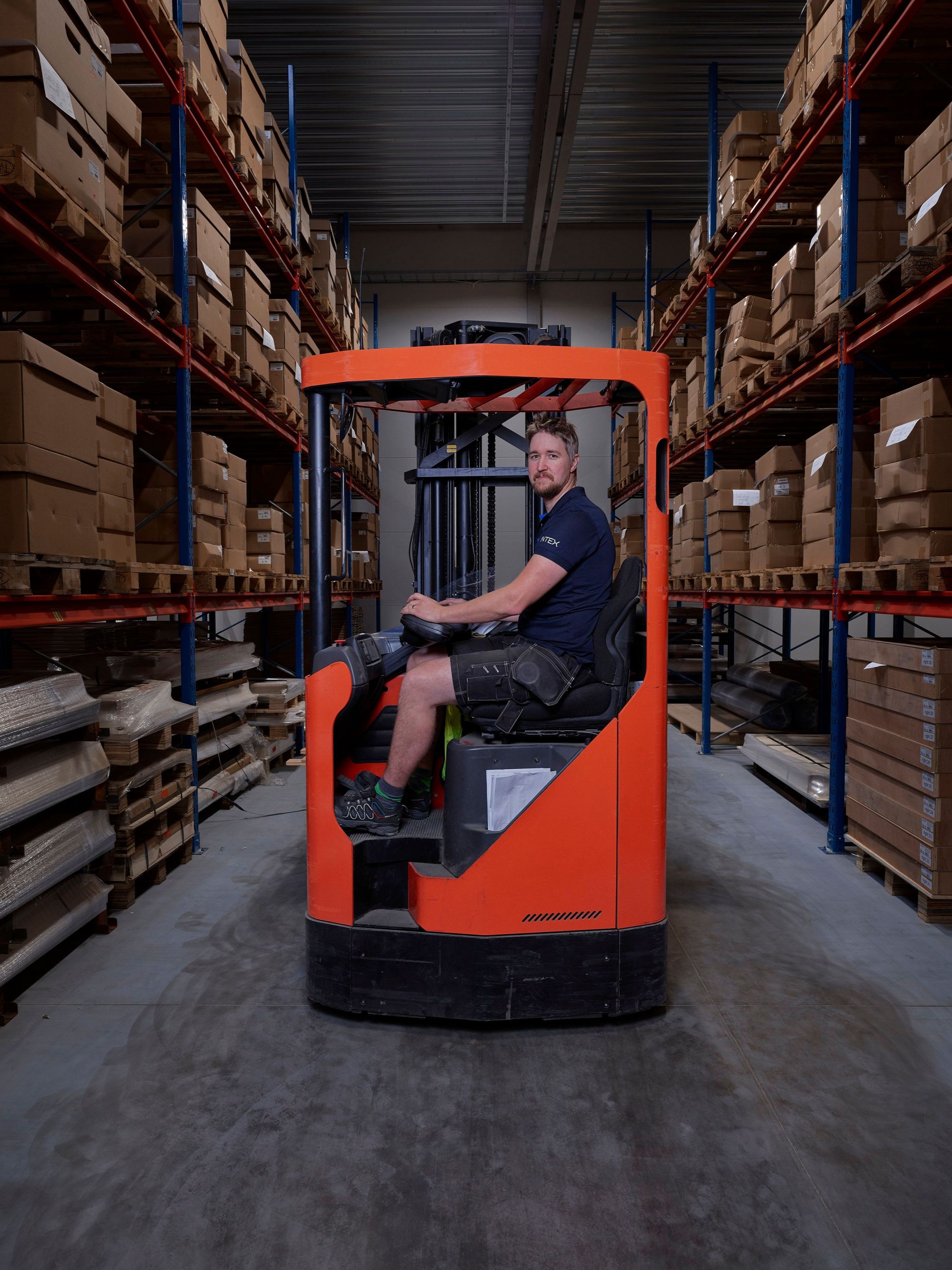 A worker on a forklift between racks of stored material