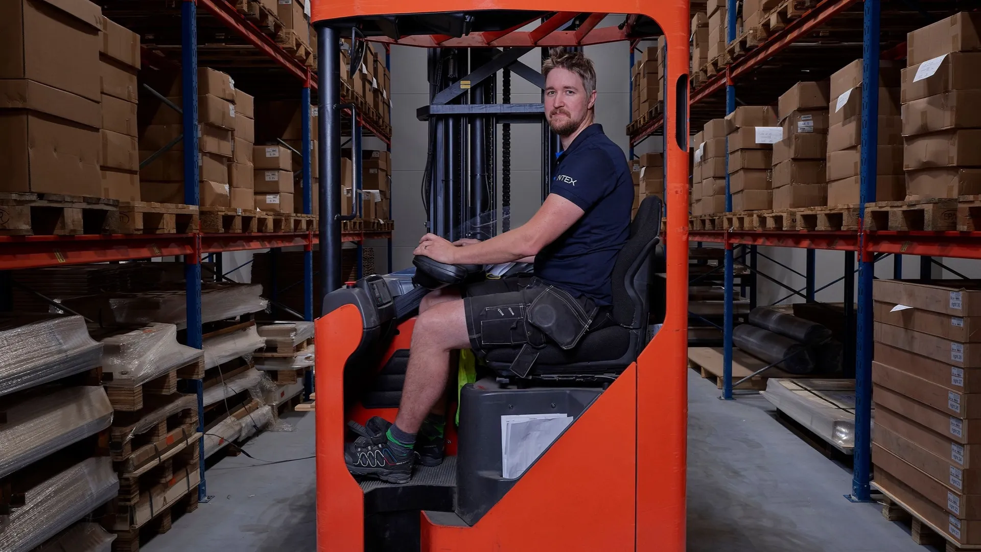 Un ouvrier sur un chariot élévateur entre des racks de matériaux stockés