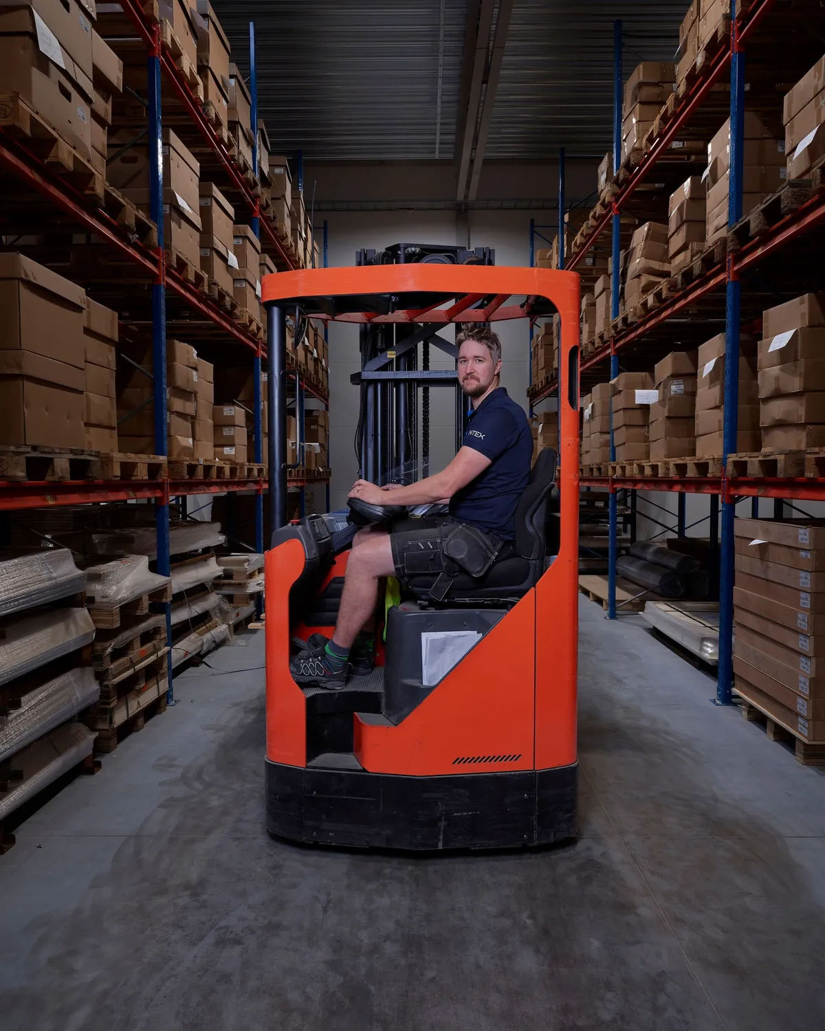 A worker on a forklift between racks of stored material