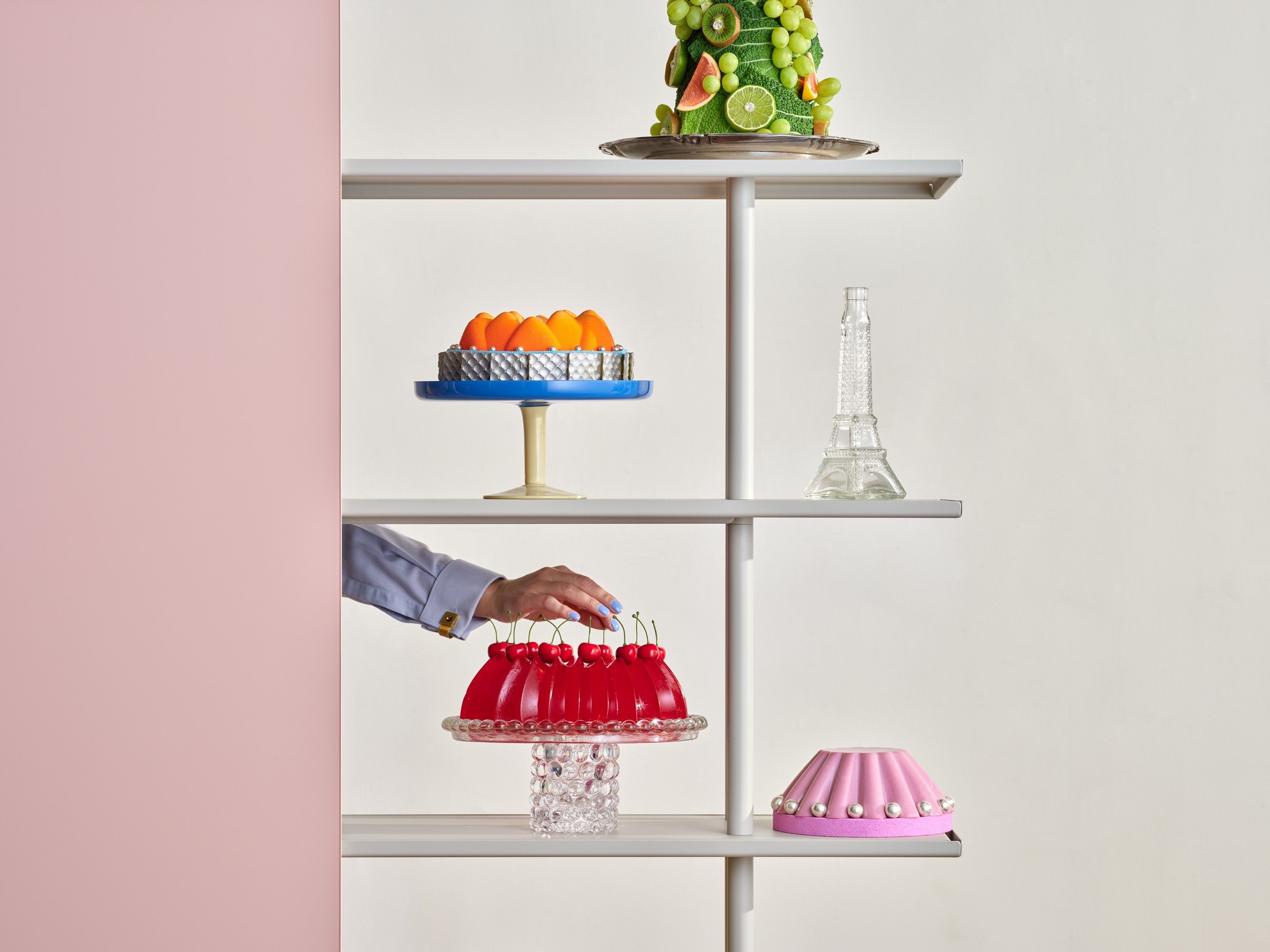 A hand placing a red jelly cake on an A08 shelf beside other pastries