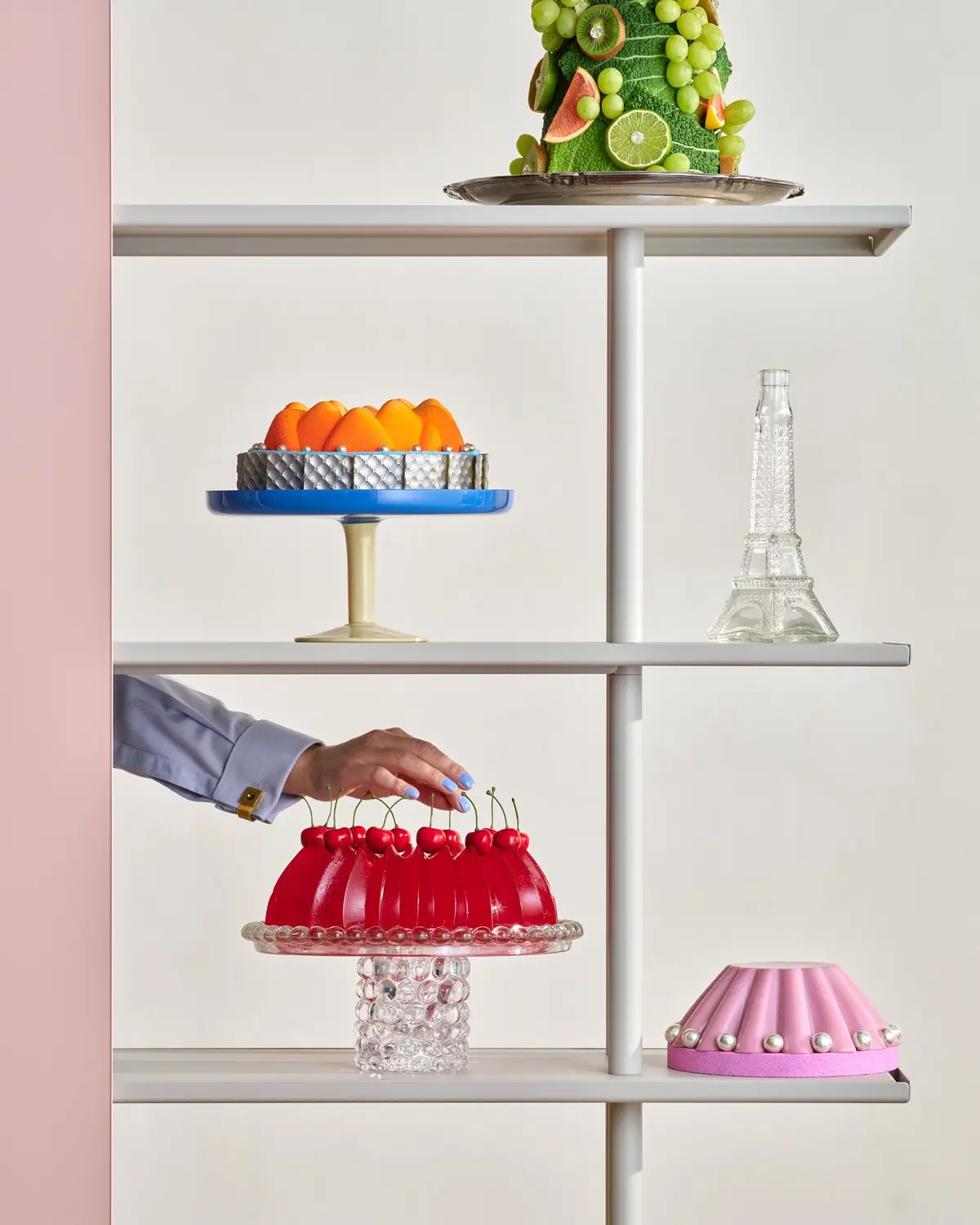 A hand placing a red jelly cake on an A08 shelf beside other pastries