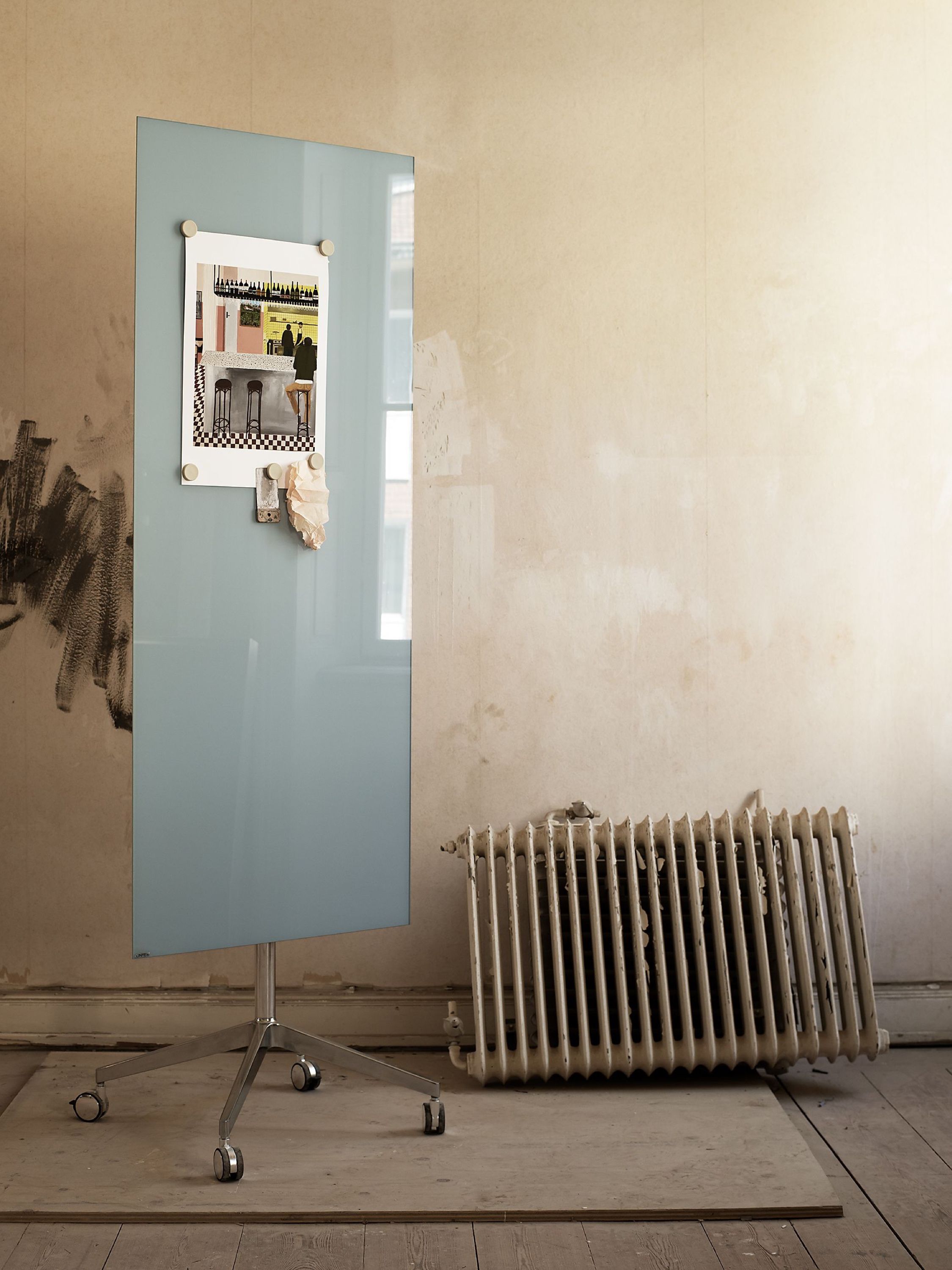 A pale blue mobile glass board with a pinned photo, next to an old radiator
