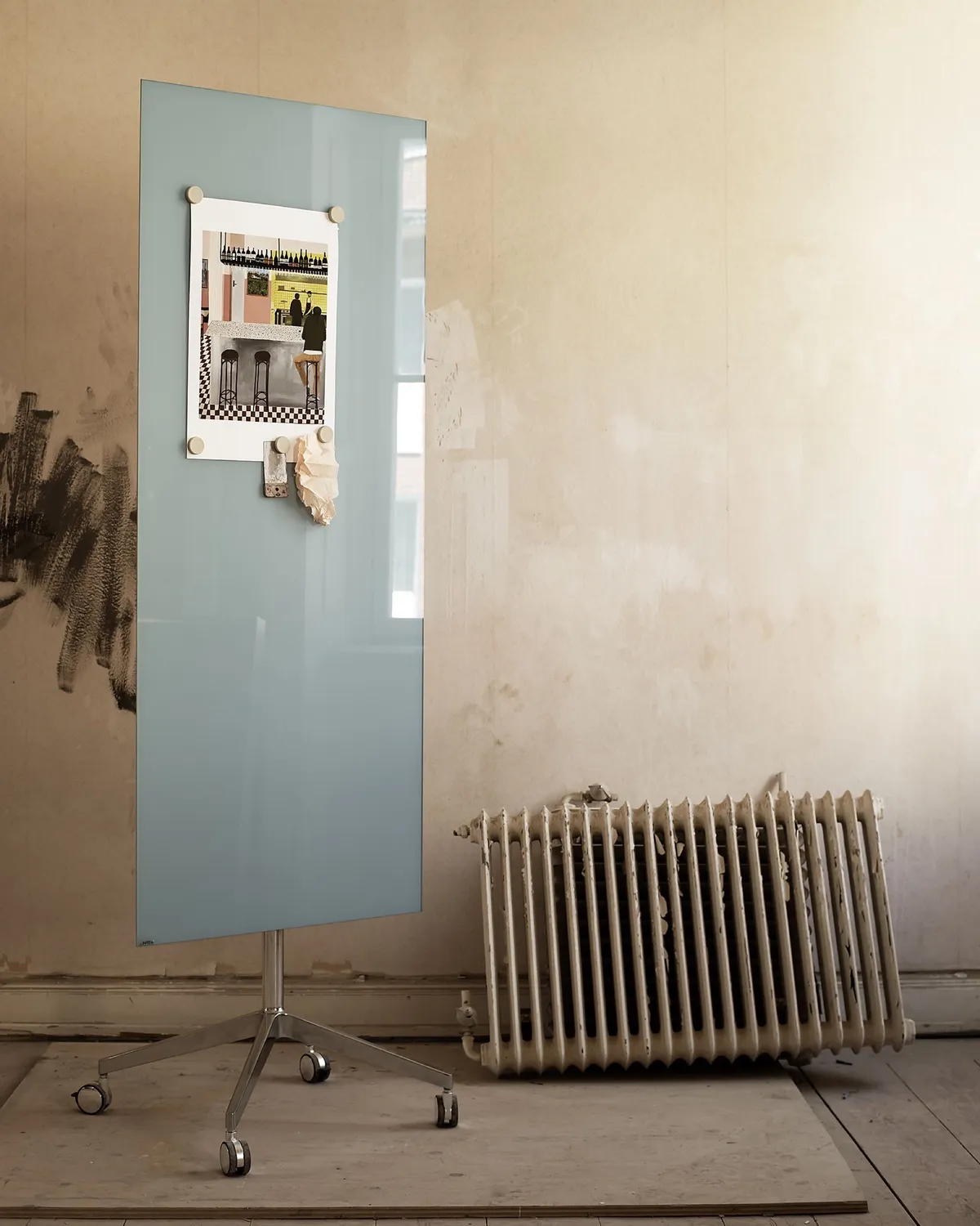 A pale blue mobile glass board with a pinned photo, next to an old radiator