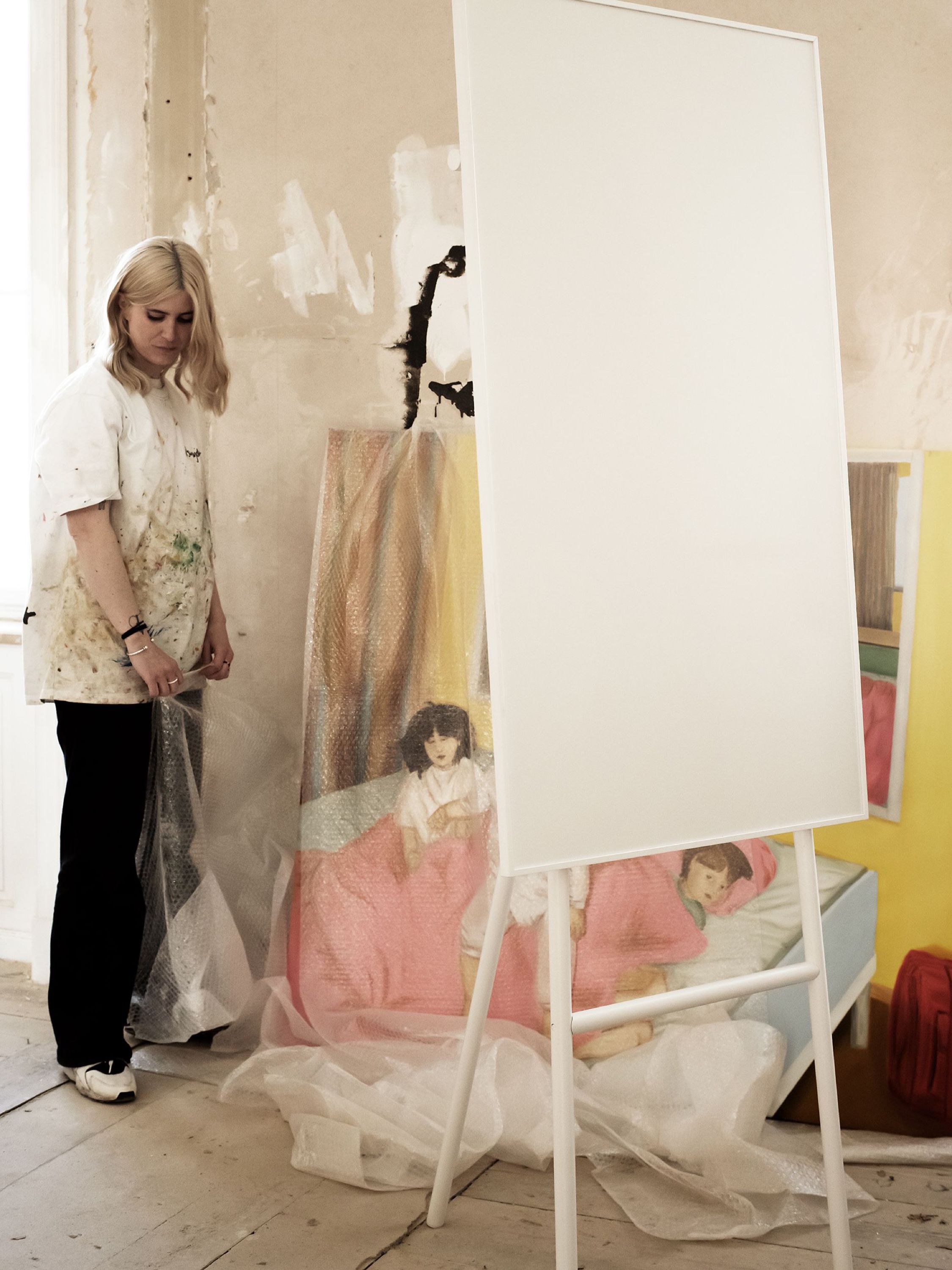 Artist Viola Sparre standing beside a mobile writing board in front of a painting