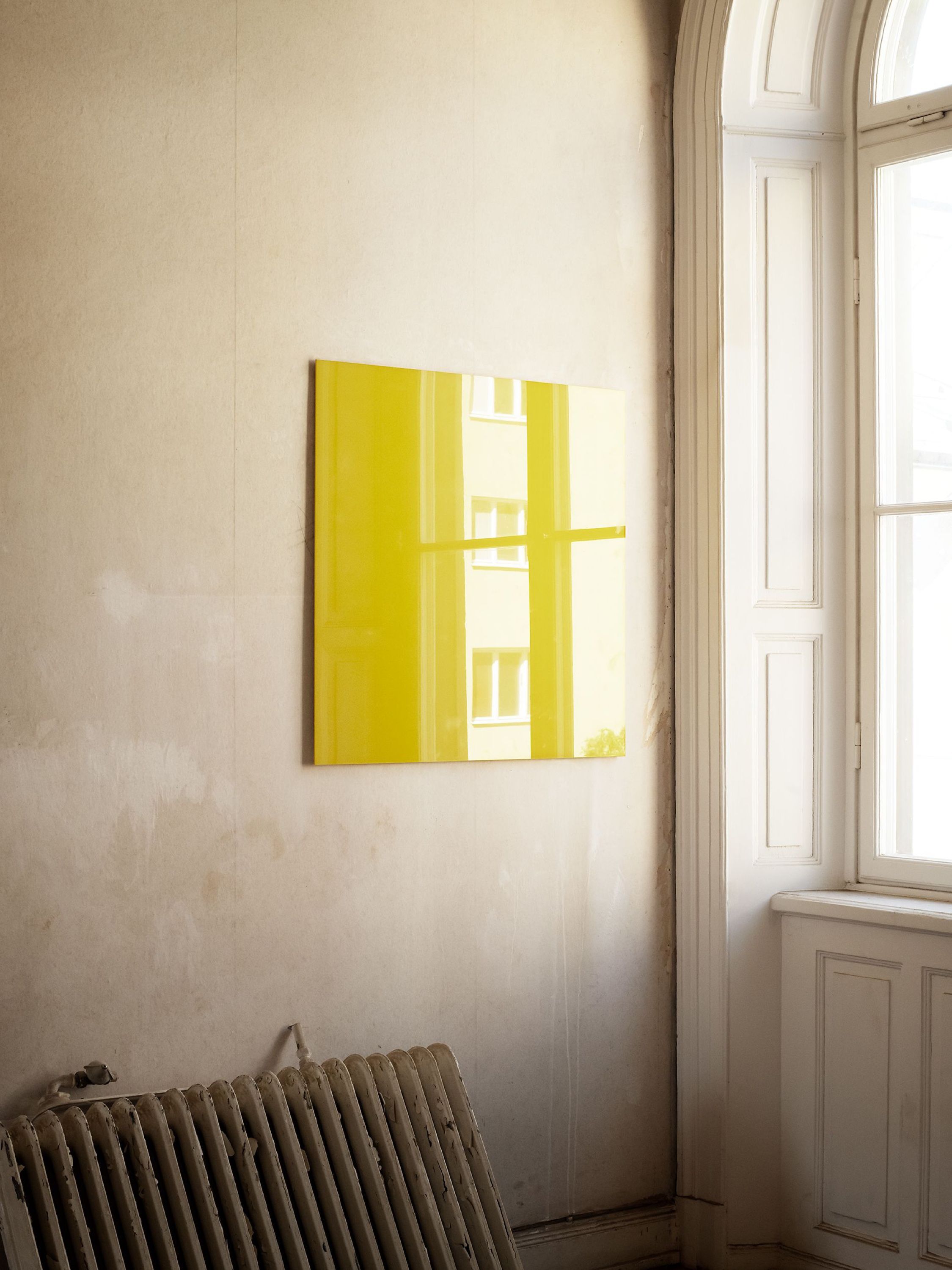 A yellow glass board on a bare wall beside a tall window