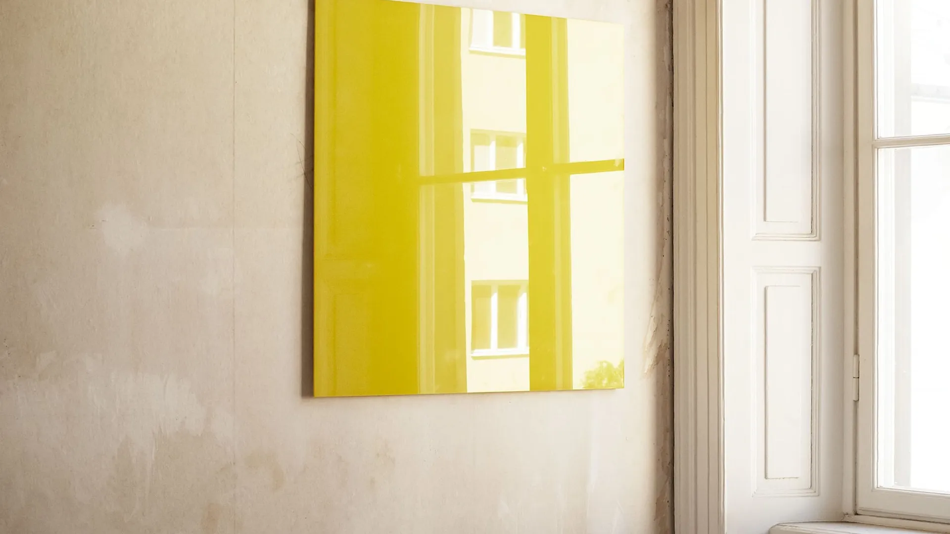 A yellow glass board on a bare wall beside a tall window