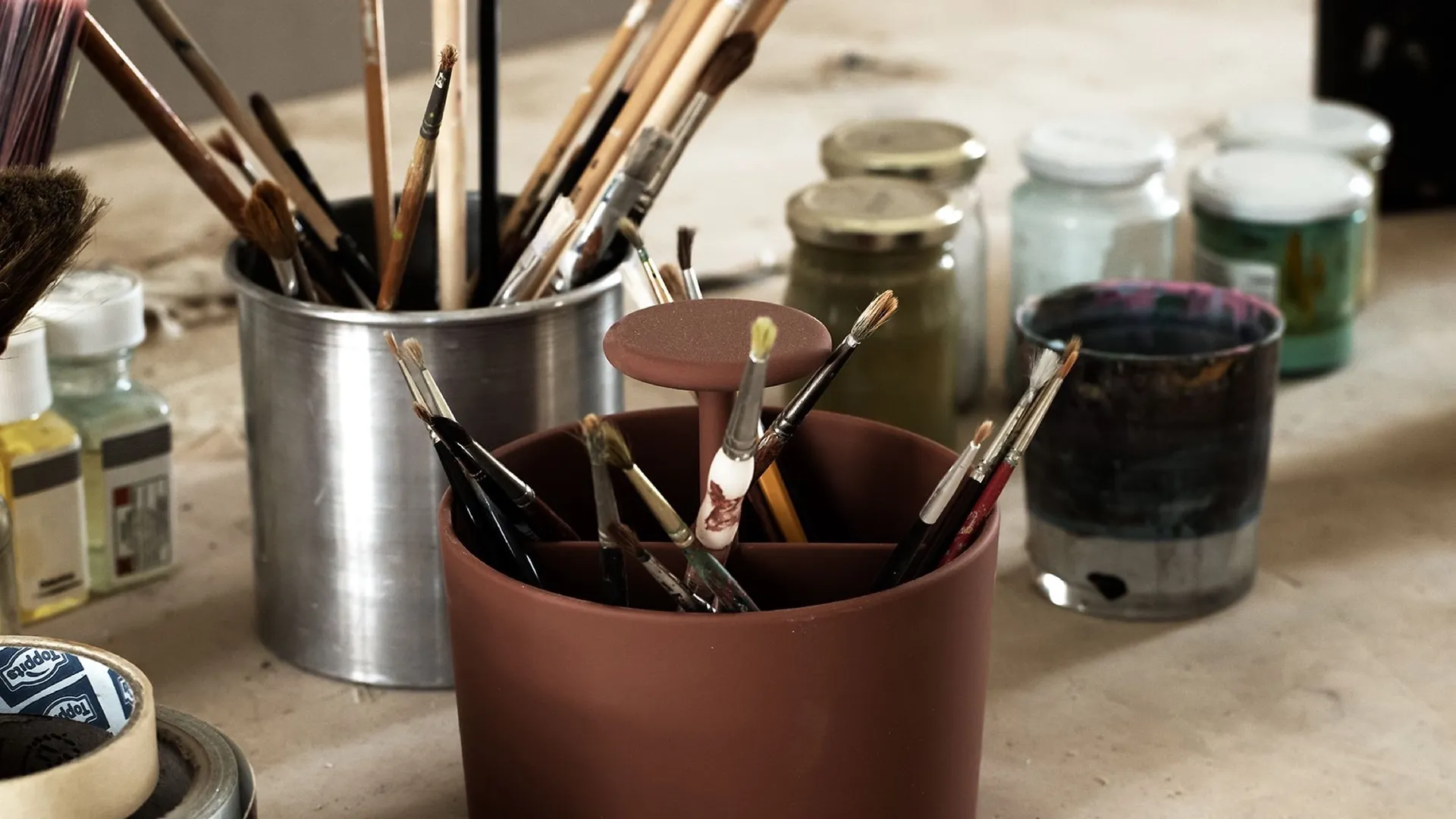 Paintbrushes in jars and pots on a work table