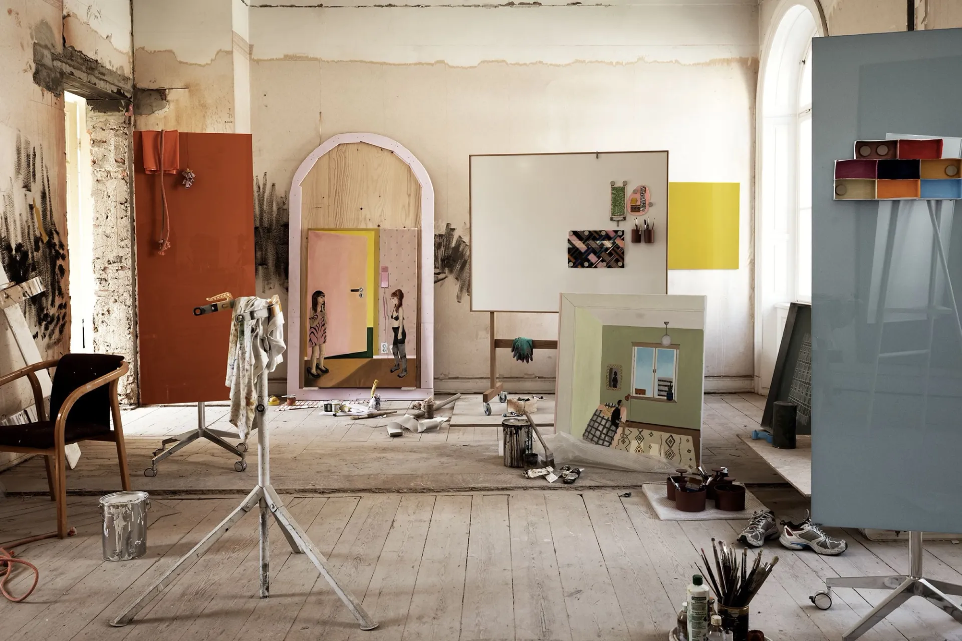 A worn artist’s studio with mobile writing boards, paintings and a chair