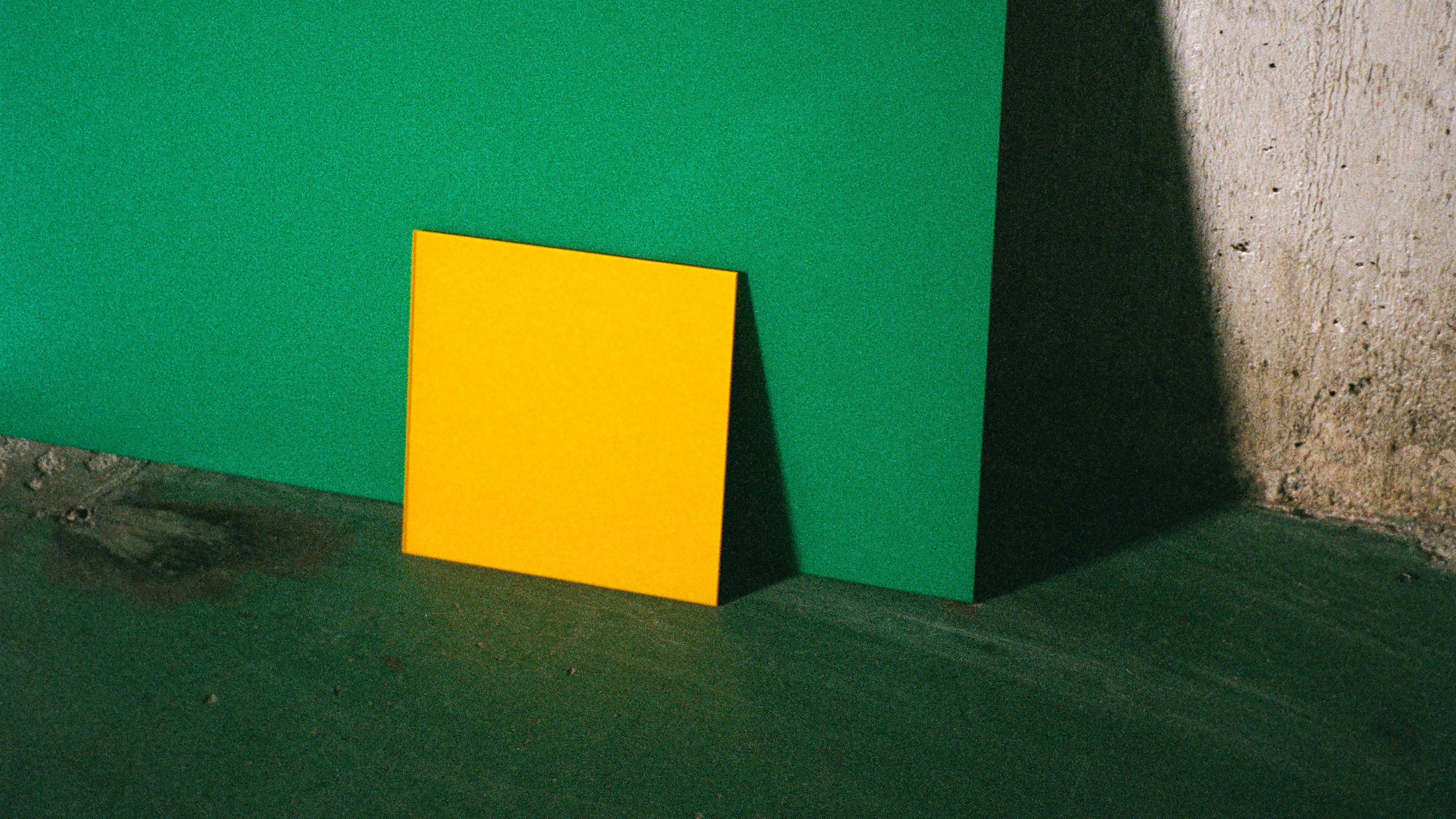 A yellow panel leans against larger green panels beside a concrete wall.