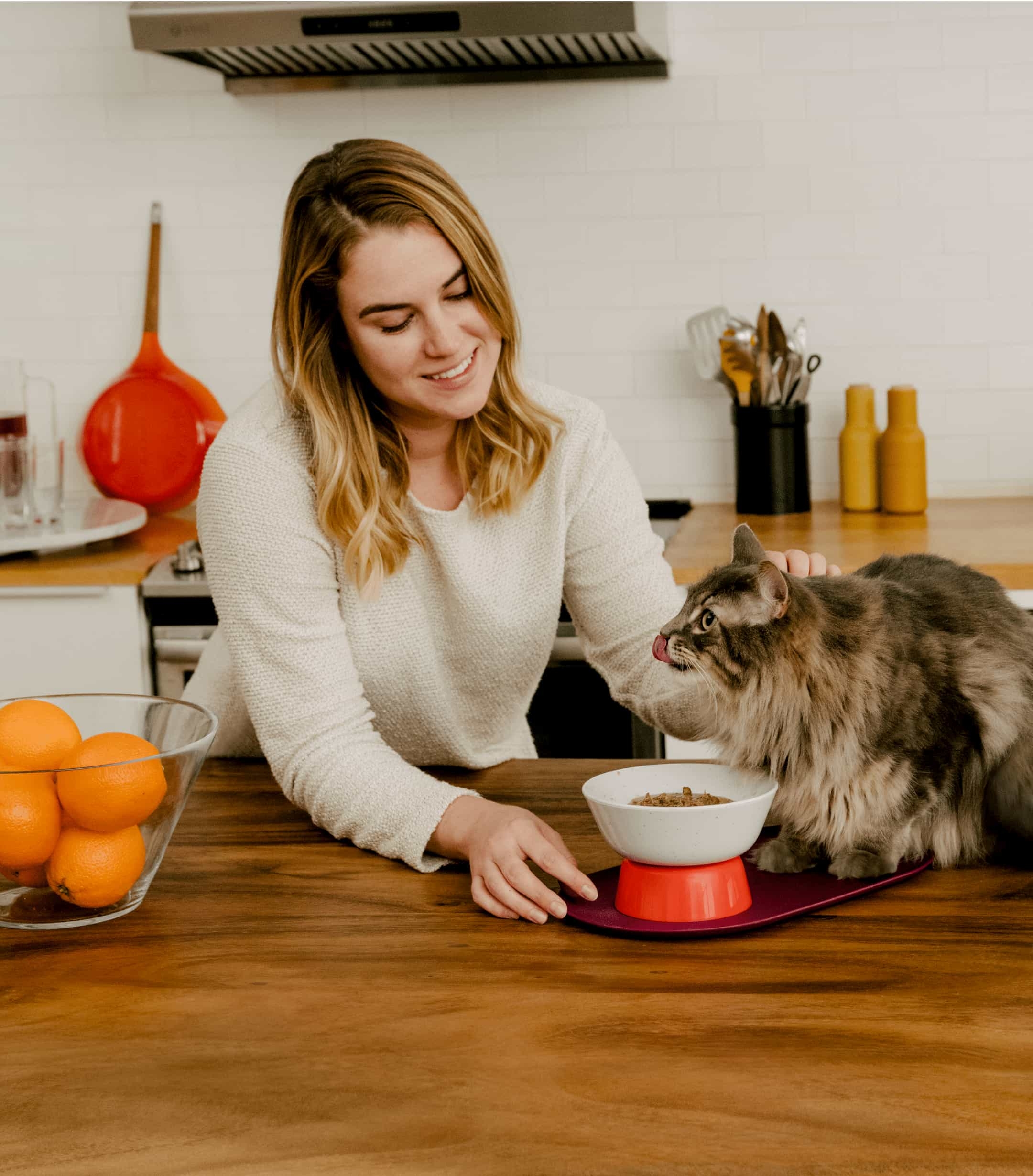Smiling woman petting cat eating wet food from Cat Person Mesa Bowl on kitchen counter