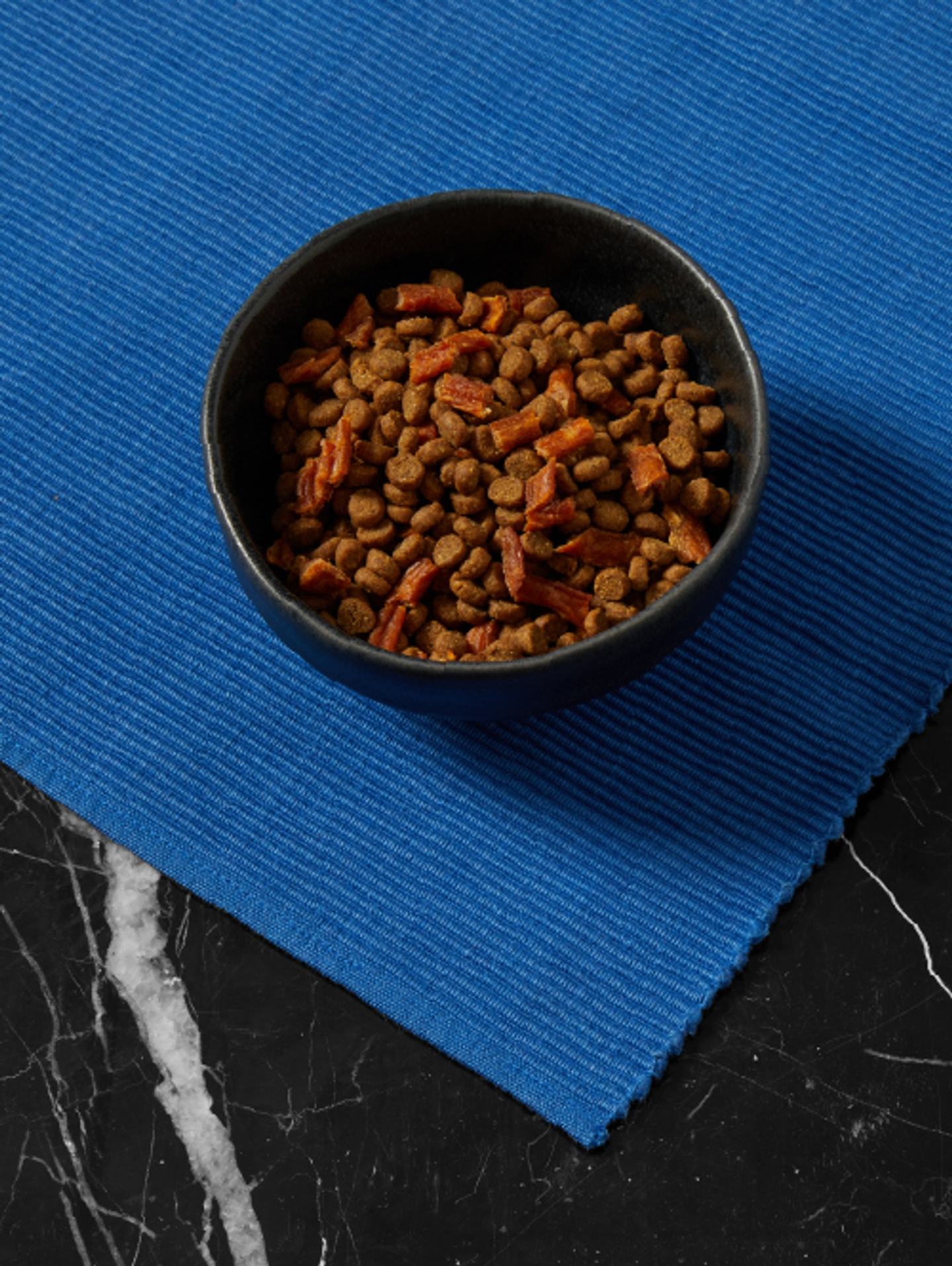 Bowl of Cat Person chicken & turkey dry food with chicken bites on blue placemat