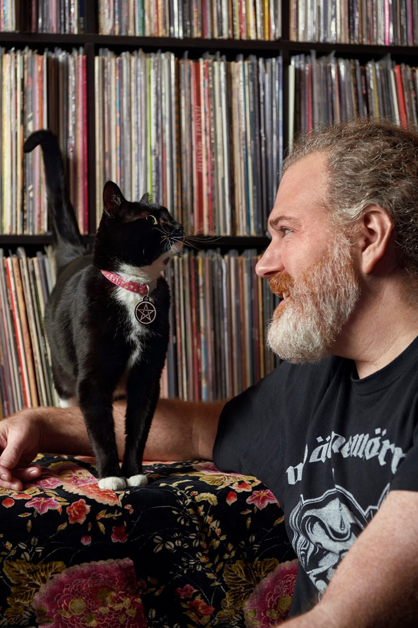 A man and his cat staring at each other lovingly in front of an expansive record collection