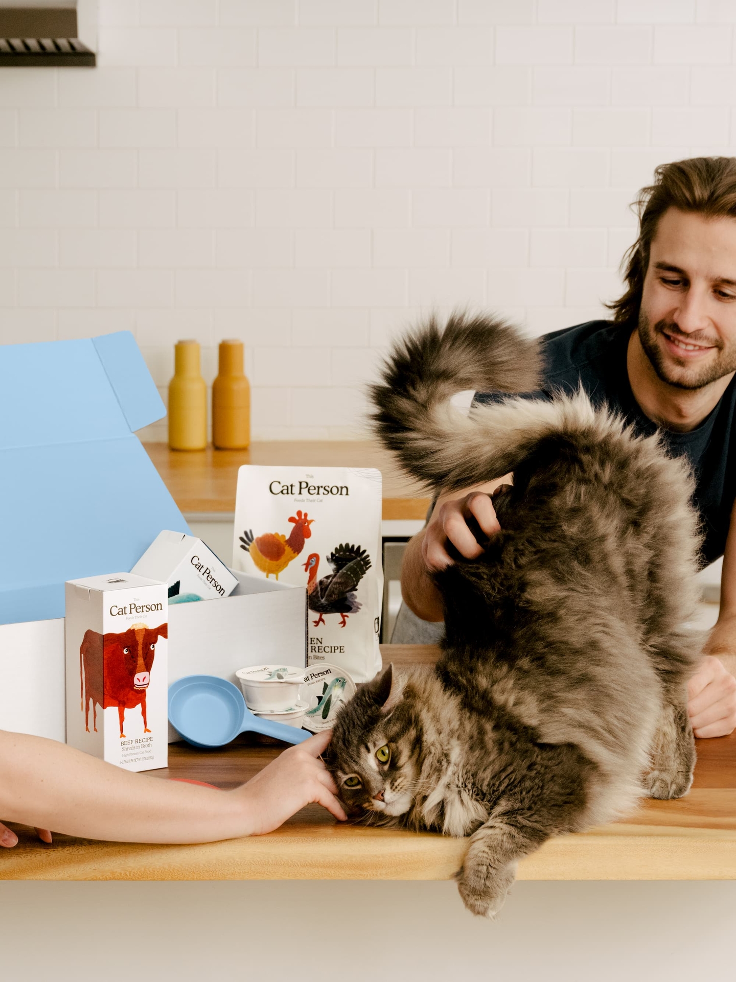 A man pets a happy cat. There is a Cat Person starter box in the background