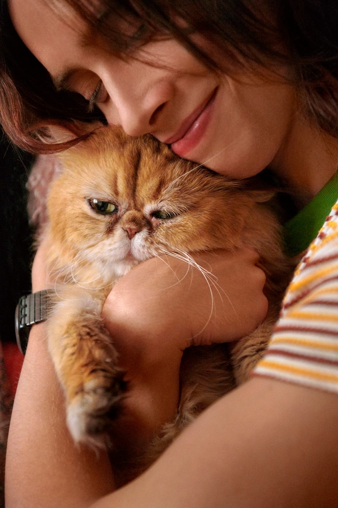 Man with long hair smiling and hugging his fluffy orange cat