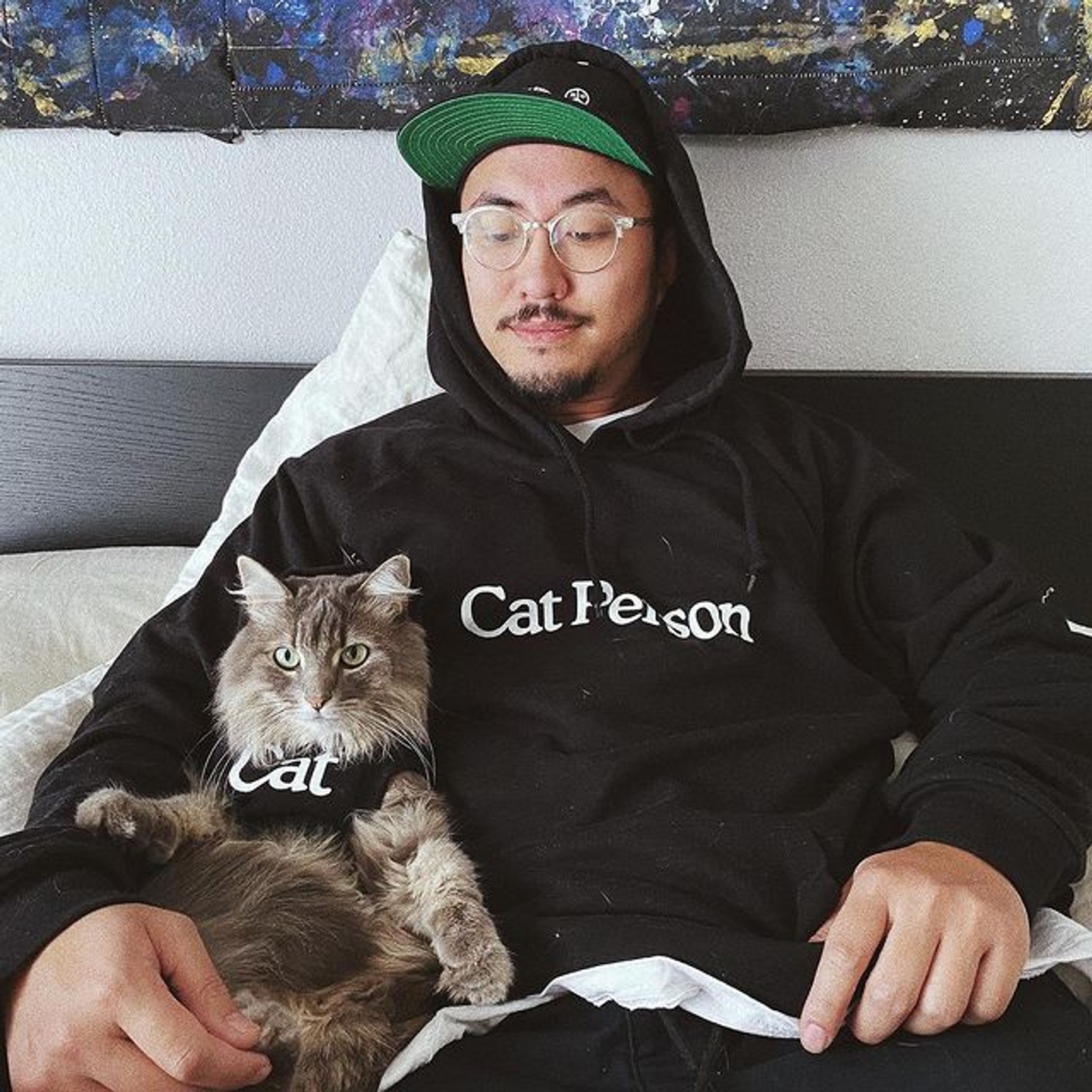 Man wearing Cat Person hoodie looking at cat wearing a cat shirt
